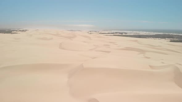 Drone flies over large sand dunes next to the ocean