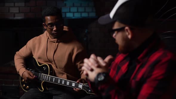 AfroAmerican Musician Guitarist Playing Guitar and Talking to Bearded Caucasian Sound Producer