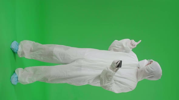 Man Wear Protective Uniform PPE And Use Mobile Phone With Point To The Side In Green Screen Studio