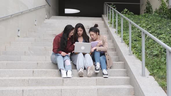 Group of Asian female students using a laptop and studying together on the stair