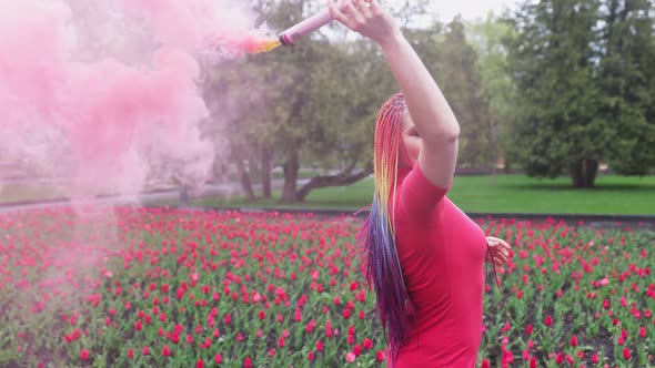 A Girl with Makeup with Rainbow Braids in Red Dress Posing in Red Smoke Against the Background of a