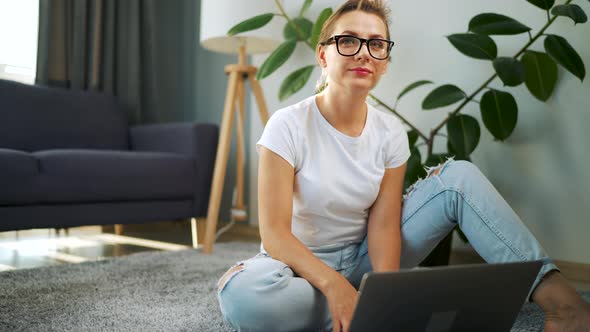 Portrait of a Woman with Glasses Looking at the Camera Over a Laptop in the Interior of a Cozy