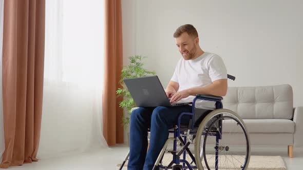 Disabled Person Freelancer is Working with Laptop Typing Sitting in Wheelchair at Home