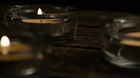 Tea candles with flaming wicks on a wooden background - CANDLES 012