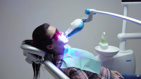 Young Woman with an Expander in Mouth and Red Protective Glasses Getting UV Whitening at the Dentist