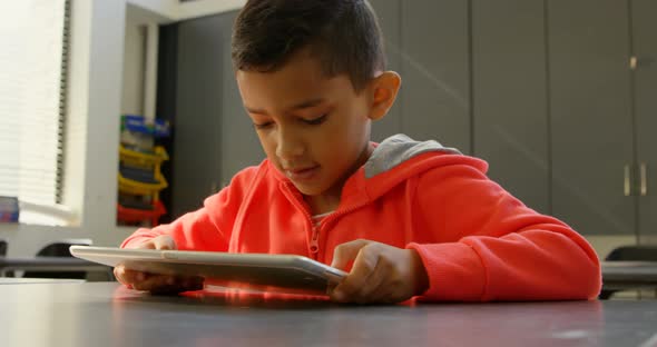 Front view of attentive Asian schoolboy studying with digital tablet in classroom at school 4k