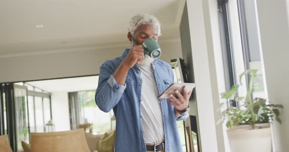 Video of african american senior man drinking coffee and using tablet