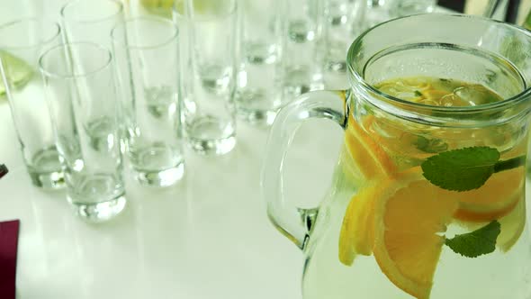 Jug of Water with Lemon and Several Empty Glasses on the Table in Restaurant