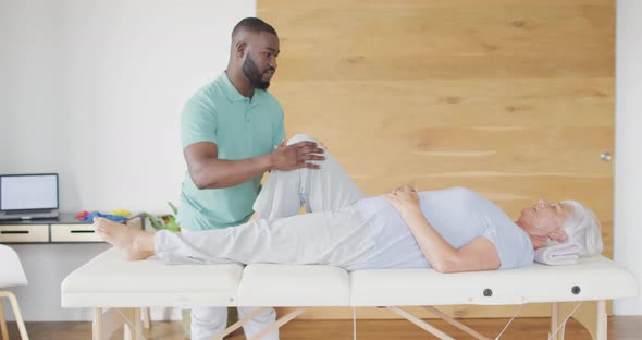 Video of african american male physiotherapist exercising with caucasian senior woman