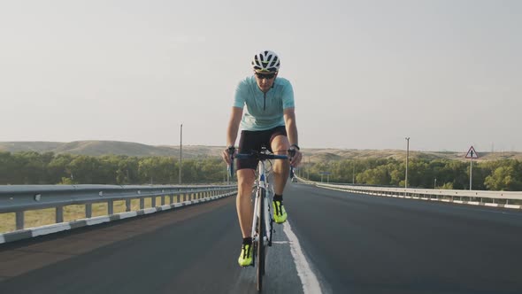 Confident Male Cyclist Rides a Road Bike on the Road Up the Mountain, Front View. A Guy Rides a Bike