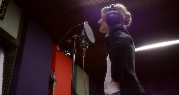 Caucasian Woman Stands with Her Back and Sings a Song in a Recording Studio