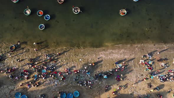 Aerial top down, Vietnamese fishing villagers crowded on beach shore. Round coracle boats moored