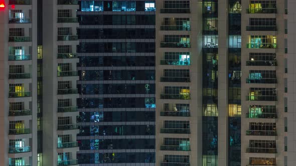 Rows of Glowing Windows with People in Apartment Building at Night