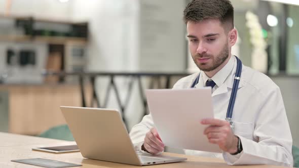Serious Doctor Working on Laptop with Documents in Office 