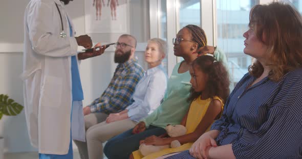 Doctor with Clipboard Inviting African Woman with Little Daughter in Office