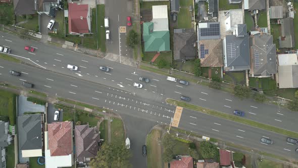 Top down aerial of cars drive at cross road in suburban highway. Featuring properties with colorful