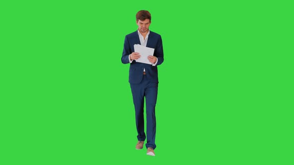 Serious Businessman Reading Documents or Report While Walking on a Green Screen, Chroma Key.