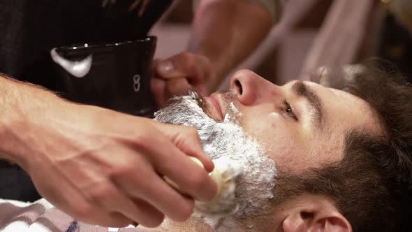 Man getting his beard shaved with shaving brush in barber shop