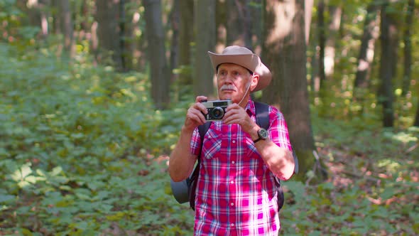 Senior Man Grandfather on Hiking Trip Exploring Wildlife Taking Photos in Forest with Retro Camera