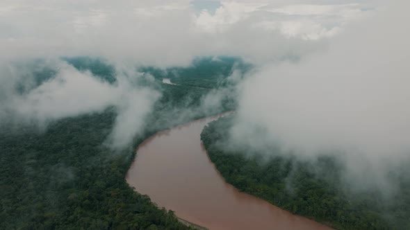 River cuts through tropical rainforest; drone view from clouds