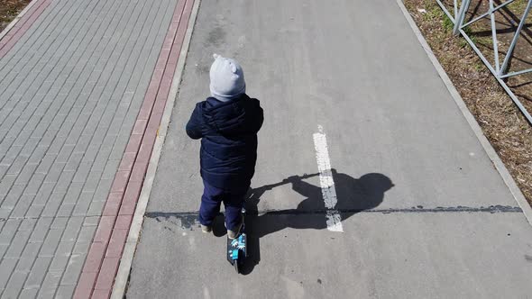 Little Boy Riding a Scooter on a City Bike Path in Early Spring