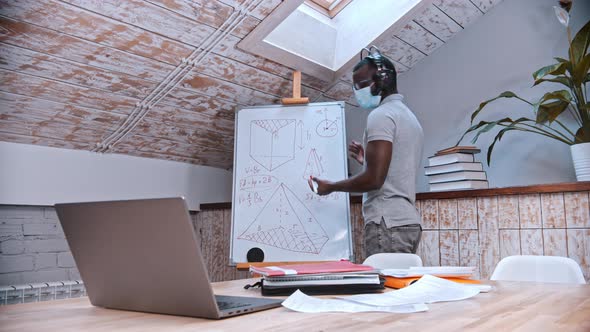 An Online Maths Lesson - an African-american Man Teacher in Medicine Mask Standing By the Board and