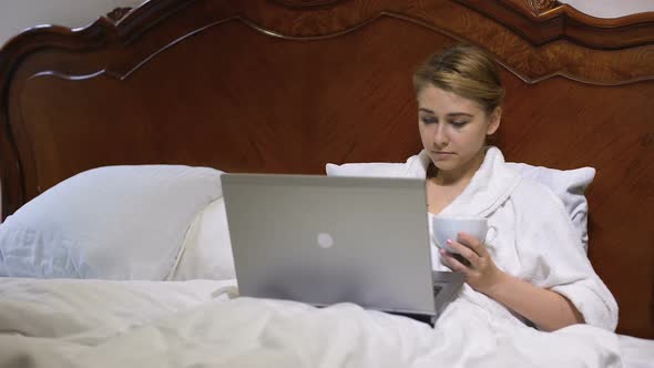 Young Business Woman Drinking Coffee in Bed and Working on Laptop, Project