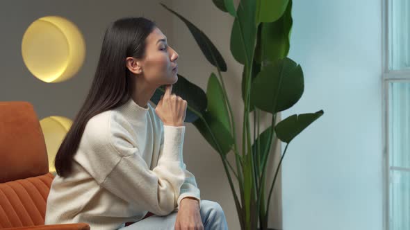 An Asian Young Woman is Sitting Inside the House and Looking Out the Window While Sitting on a Chair