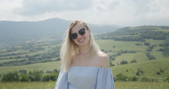 Beautiful Girl in Sunglasses Is Smiling and Looking at the Mountains. Sunny Day. Beautiful Mountains