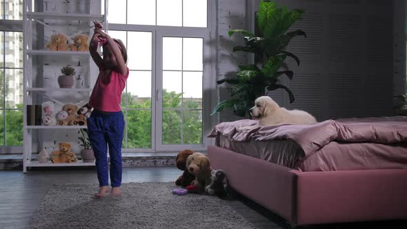 Cute Little Girl Dancing for Puppy Lying on Bed