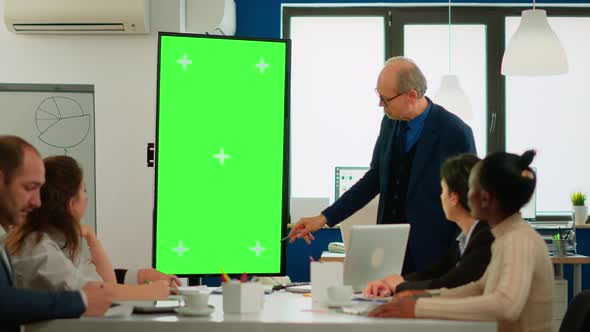 Mature Businessman Analysing Reports Standing in Conference Room Pointing at Green Screen...