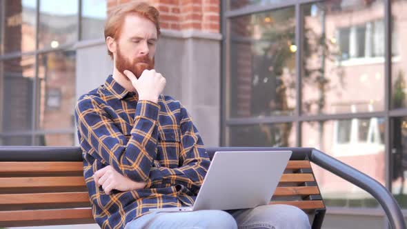 Pensive Redhead Beard Young Man Working on Laptop Sitting Outdoor on Bench