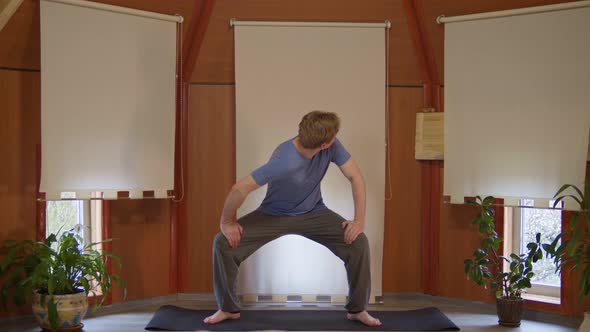 Front View of Young Male Standing on Yoga Mat Stretching Neck and Shoulder Parts Indoors