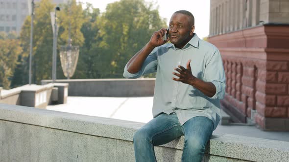 Adult Mature African American Man Sitting Outdoors Holding Cell Phone Irritably Angry Talking to