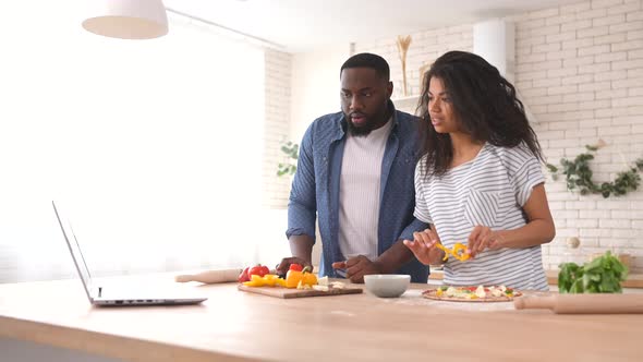 Happy Multiracial Couple Preparing Meal Together in Front of a Laptop