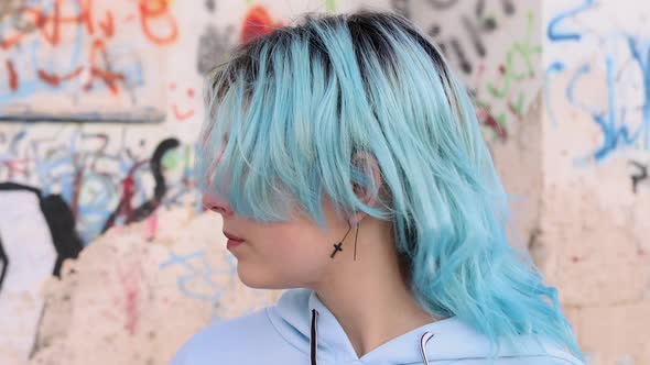 Blue haired teenage girl in hoodie turning head left and right. Head portrait against graffiti wall