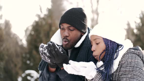 African American Couple Blowing Snow From Hands on Sunny Snowy Weather