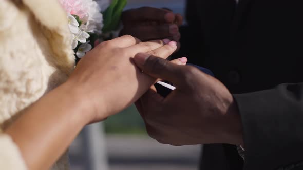 Closeup of African American Male Hand Putting Wedding Ring on Female Finger Outdoors