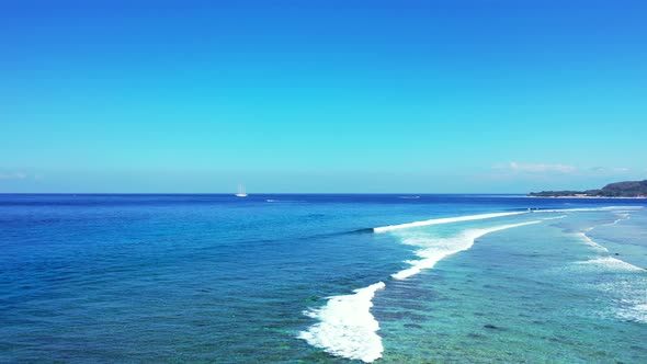 White waves of blue sea splashing over calm turquoise lagoon with coral reefs under clear bright sky