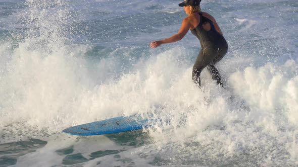 A young woman in a wetsuit surfing on a longboard surfboard.