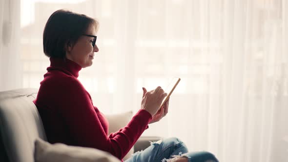 Relaxed Young Woman in Glasses Using Her Smartphone While Sitting on the Sofa