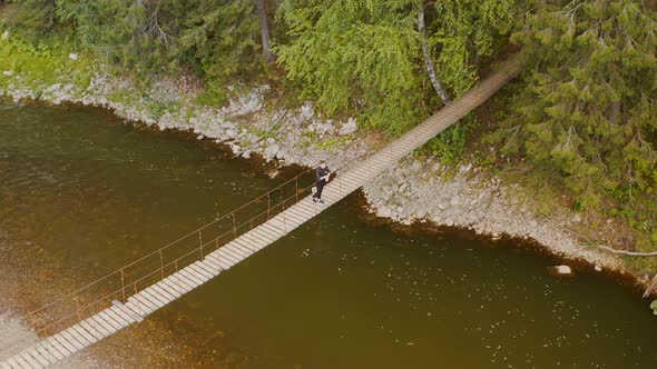 A male tourist is walks along a suspended wooden bridge on an summer evening