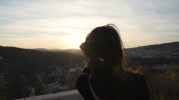 Girl with Sunglasses Enjoying the Sunset Over Scenic Landscape While Wind Blows Into Her Hair