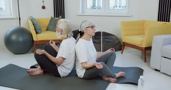 Senior Couple Sitting Back to Back in Lotus Pose During their Workout at home