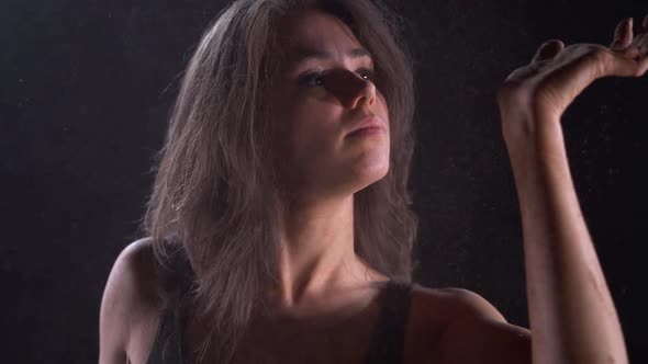 Portrait of a Young Energetic, Plastic Woman in a Black Suit in the Studio on a Dark Background