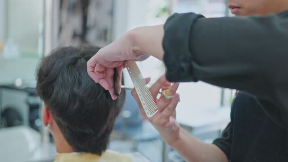 Expert male stylist's hand combing and using scissors cutting young male customer's hair in salon.