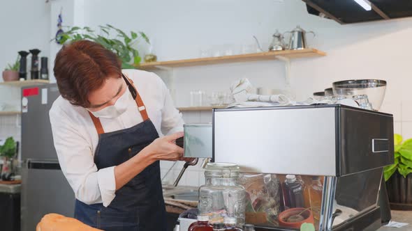 Cafe business owner wear mask due to Covid-19, check coffee maker machine on counter in restaurant.