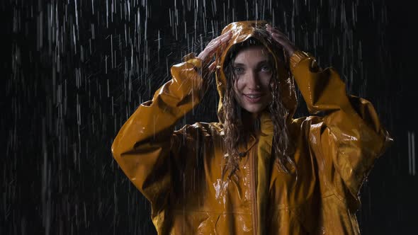 Attractive Young Woman in Yellow Raincoat Stands on the Street at Night in the Rain. Cute Girl