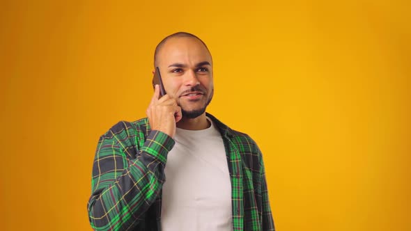 Worried Anxious Man Talking on Mobile Phone Against Yellow Background