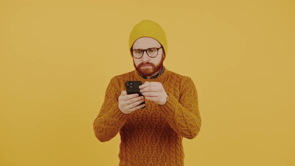 Millennial Caucasian Bearded Male Hipster in a Beanie and Knitted Sweater Angrily Scrolling Through